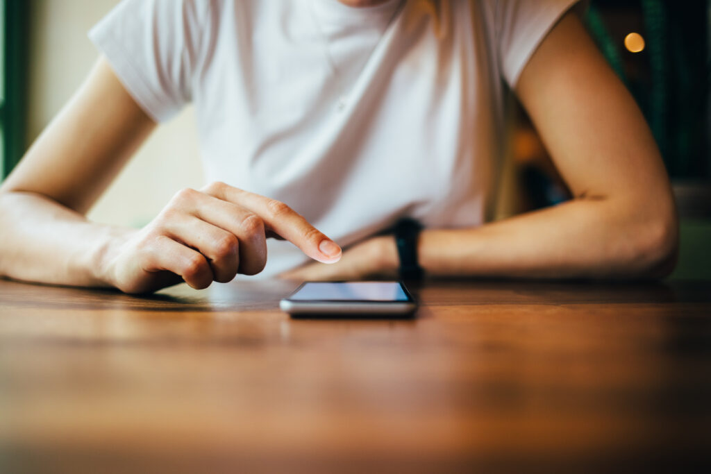 A woman searches on her smartphone as it rests on a table.